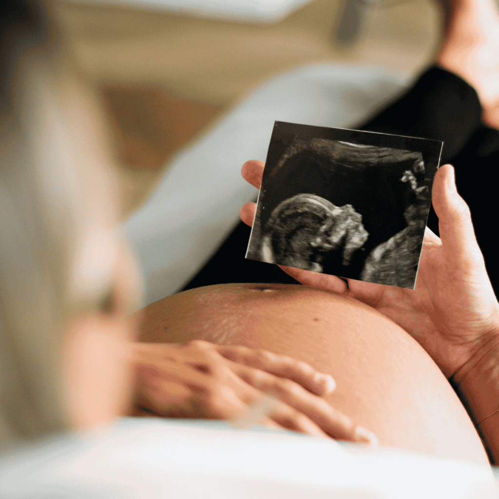 Pregnant person holding an ultrasound image over their stomach, symbolising the outcome of fertility treatments like IUI or IVF